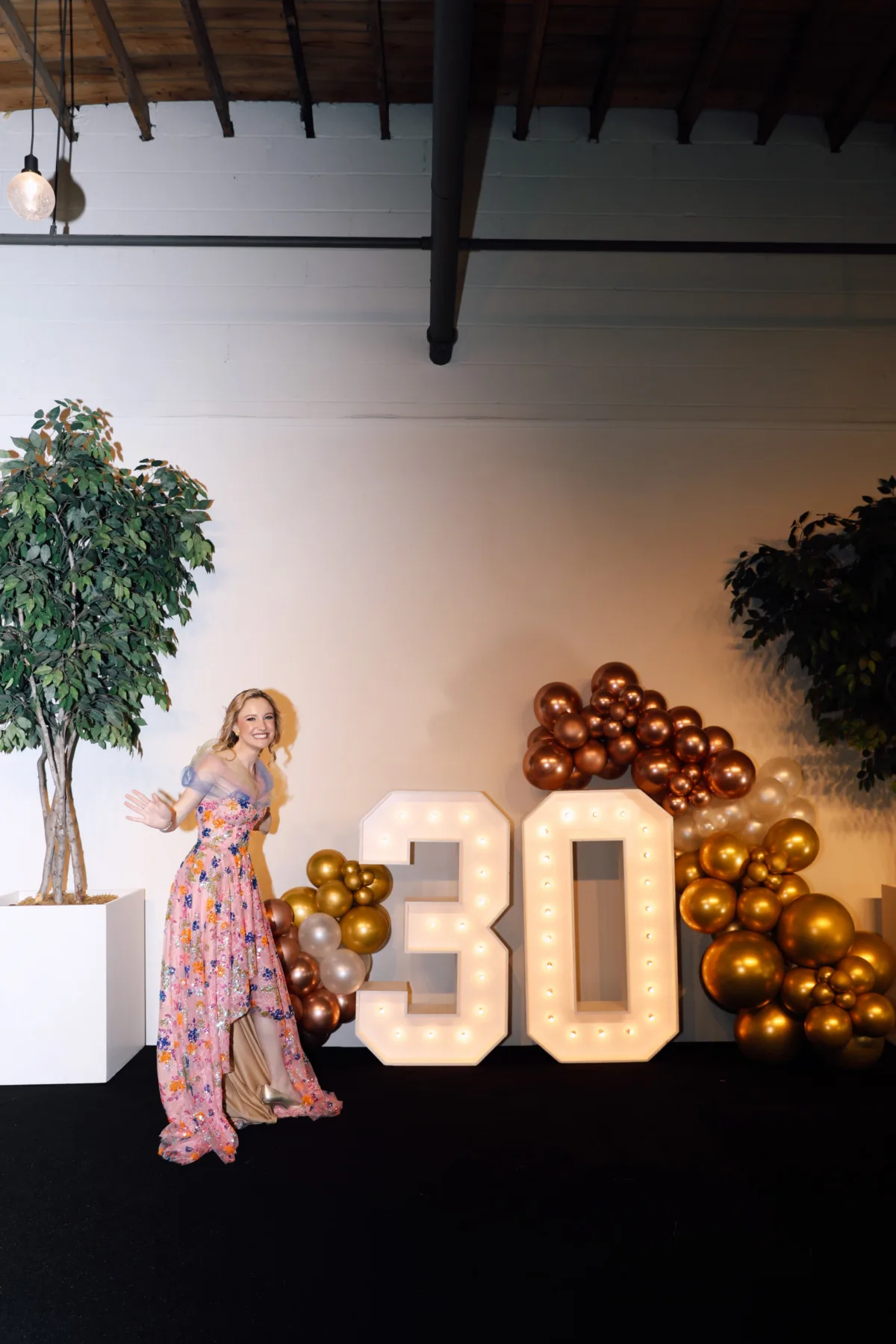 Woman celebrating her 30th birthday party with illuminated marquee numbers and bronze balloon installation at Nashville event venue