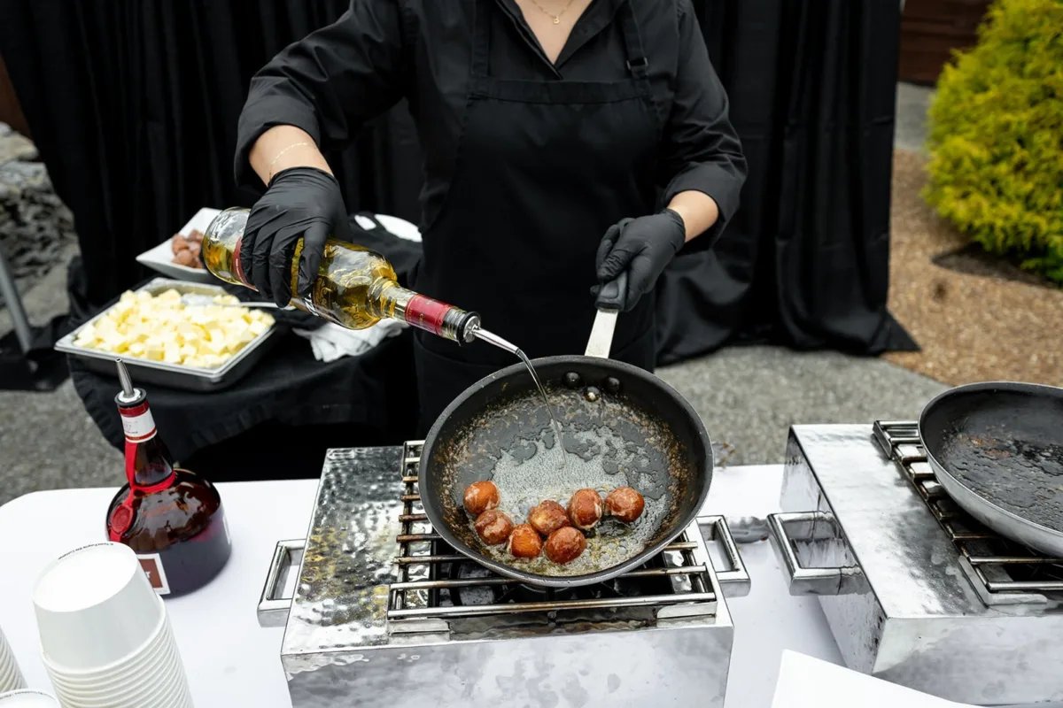 A Catered Affair chef in black gloves flambéing scallops with wine in a pan during live cooking demonstration at Nashville wedding reception