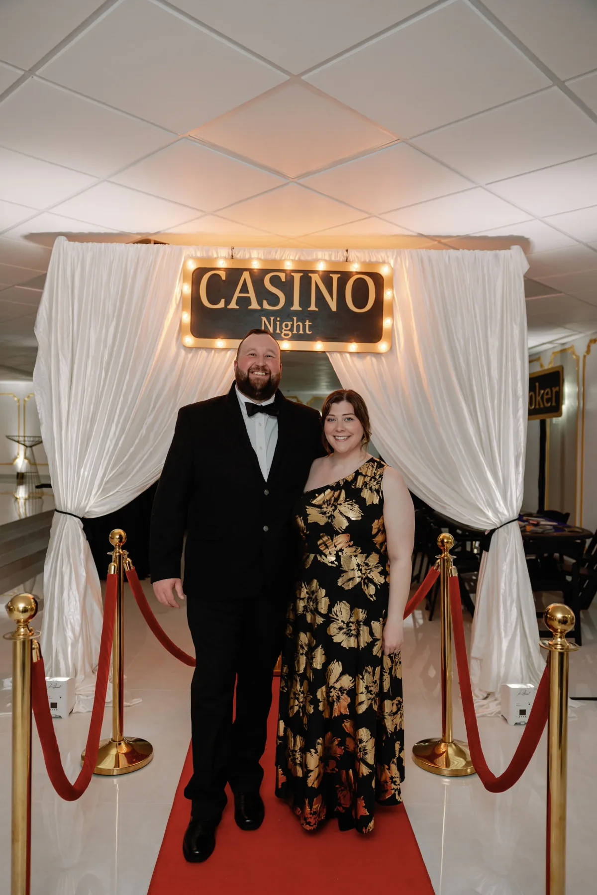 casino night private event couple red carpet entrance - Nashville Private Event Catering Couple posing at casino night private event entrance with red carpet and elegant backdrop in Nashville