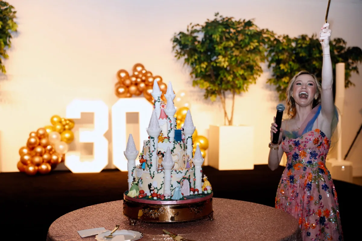 Woman celebrating with elaborate Disney castle birthday cake featuring multiple character figurines at Nashville event catered by A Catered Affair