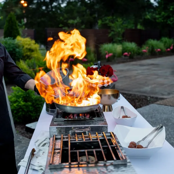 Dramatic flaming pan cooking station with chef preparing food outdoors at Nashville wedding catered by A Catered Affair