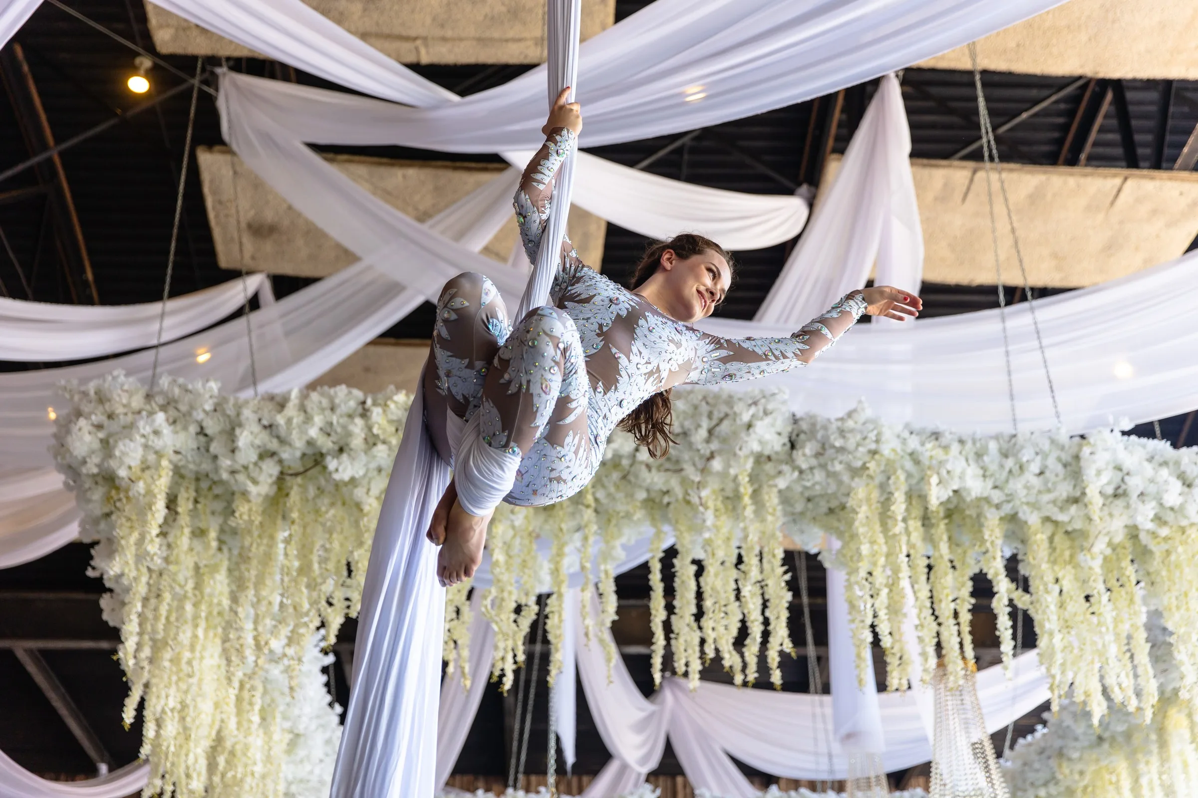 Aerial silk performer in white lace costume suspended above elaborate white floral installations at Nashville corporate event catered by A Catered Affair