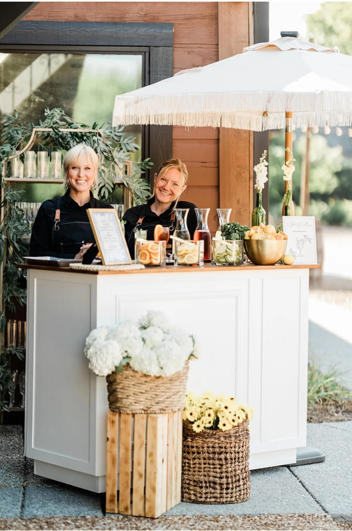 Professional bartenders from A Catered Affair serving cocktails at an elegant outdoor wedding bar station in Nashville with white umbrellas and floral decorations