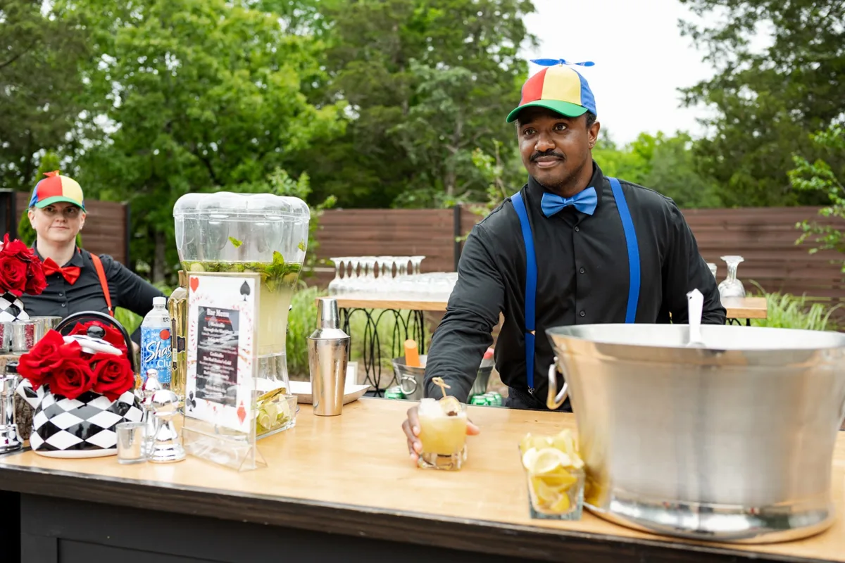 Professional bartender in colorful cap and bow tie serves cocktails at outdoor Nashville wedding reception with A Catered Affair catering