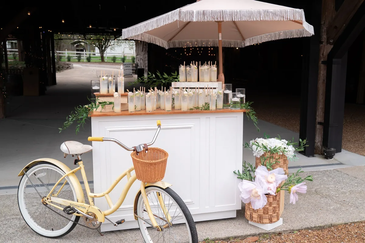 Elegant white beverage station with umbrella and vintage yellow bicycle at Nashville wedding venue by A Catered Affair