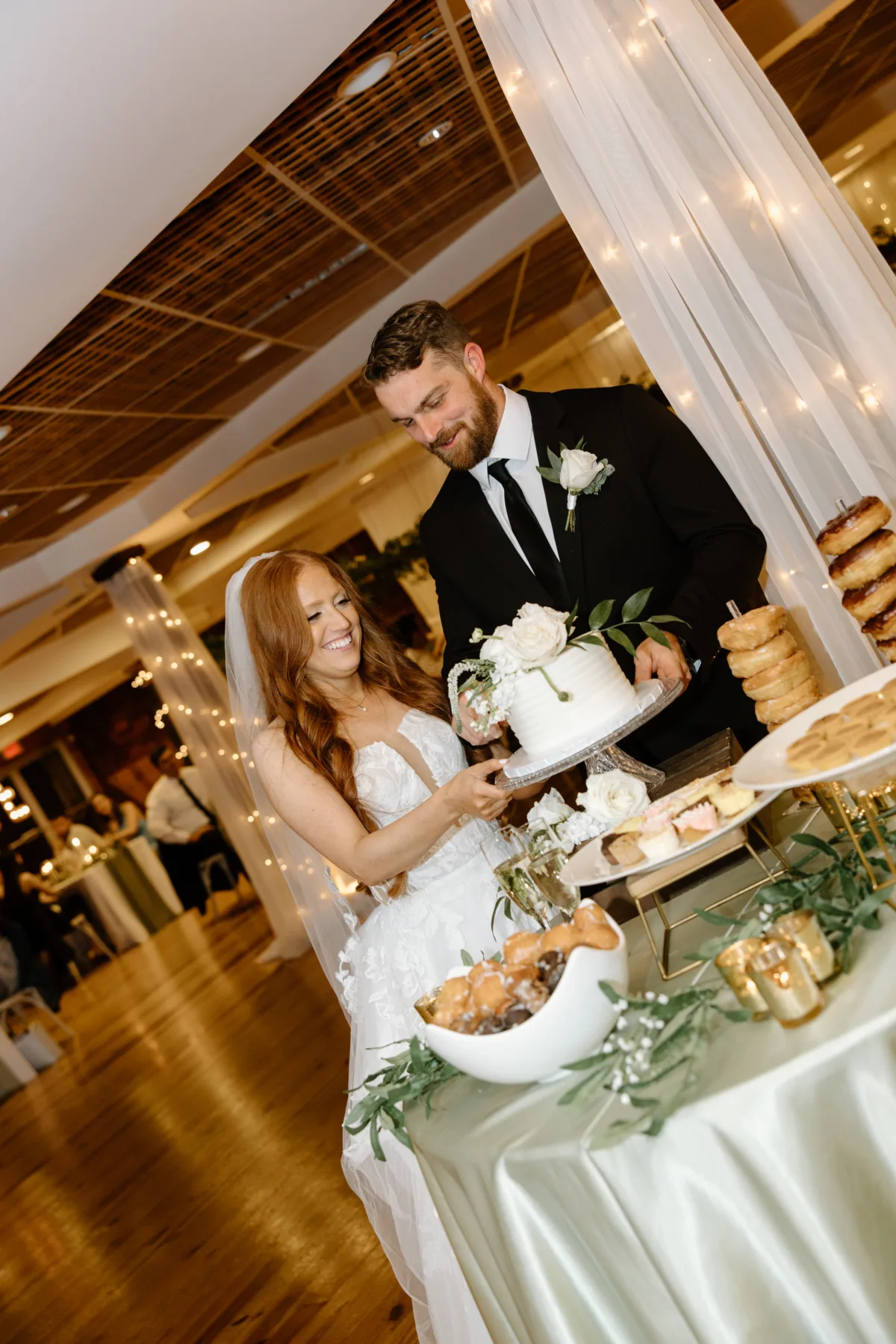 Bride and groom cutting wedding cake at Nashville reception catered by A Catered Affair with elegant dessert display and string lights
