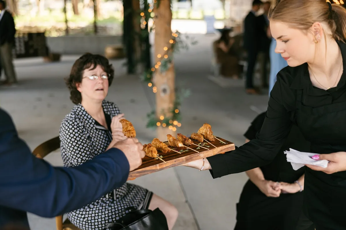 A Catered Affair server presenting elegant appetizers on wooden board to wedding guests at Nashville venue