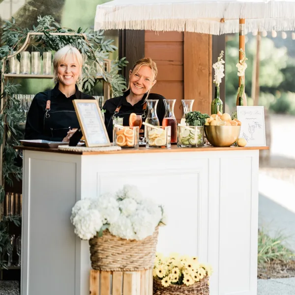 Elegant outdoor wedding bar setup with two bartenders serving drinks under white umbrella by Nashville caterer A Catered Affair