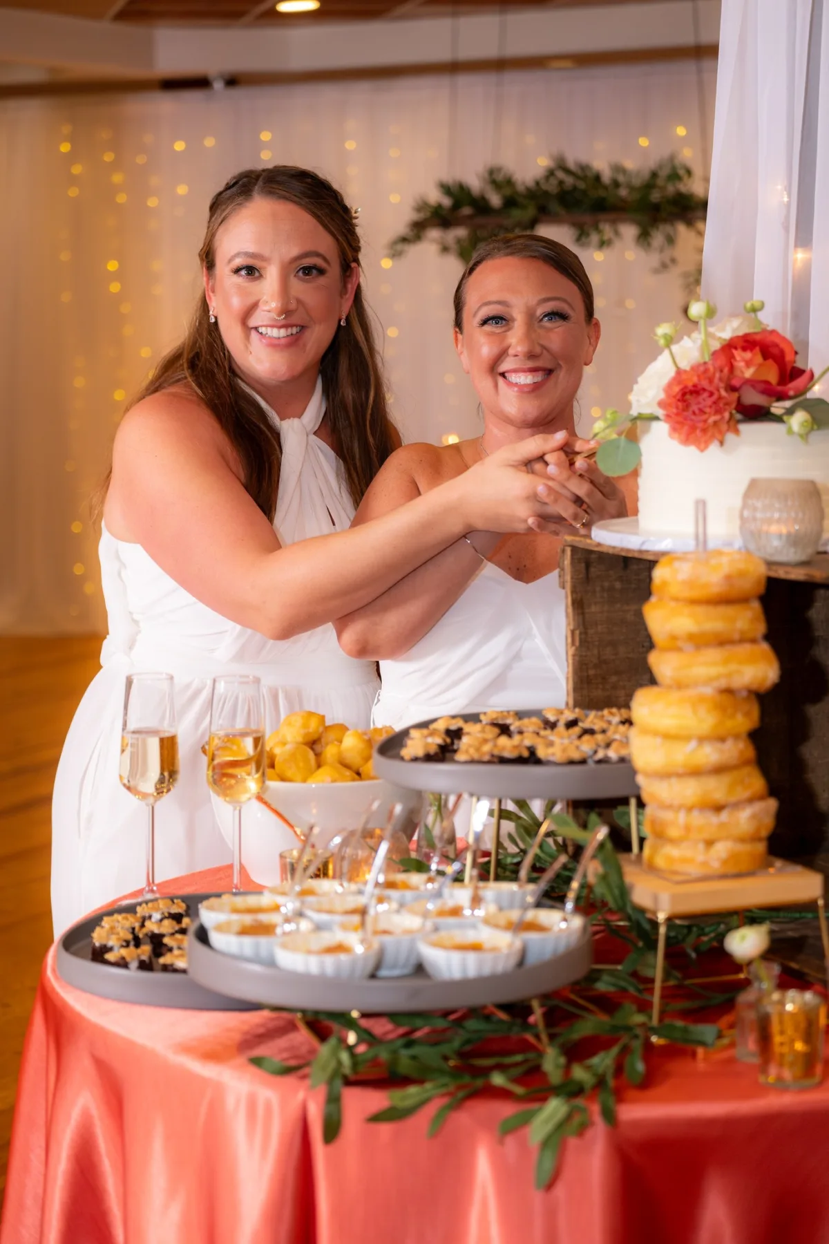 Two brides cutting wedding cake at elegant dessert station catered by A Catered Affair in Nashville with champagne and donuts display