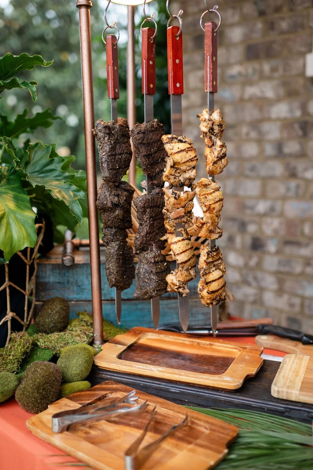 Grilled meat skewers on copper display stand for Nashville wedding catering by A Catered Affair with wooden serving boards and tropical decor