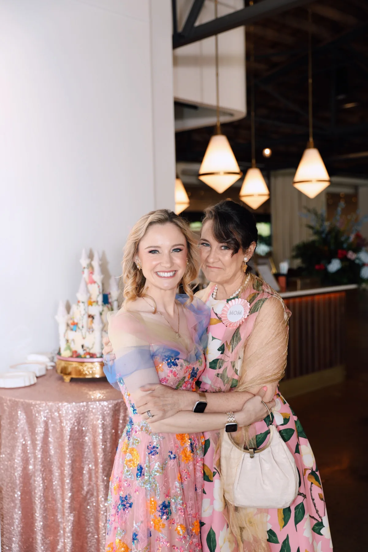Mother and daughter embracing at Nashville wedding celebration catered by A Catered Affair with elegant floral dresses and rose gold sequin linens
