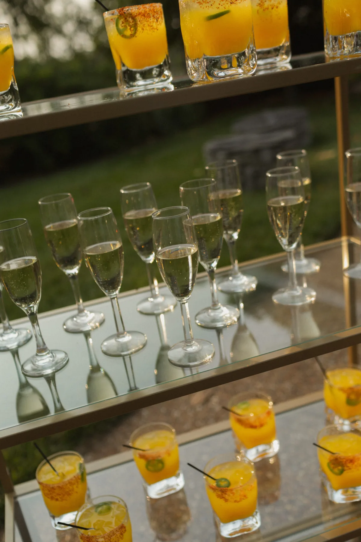 Elegant champagne flutes and orange cocktails with garnishes displayed on mirrored trays for Nashville wedding cocktail hour by A Catered Affair