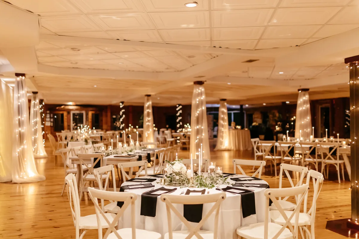 Elegant wedding reception setup with round tables, white cross-back chairs, black and white linens, and romantic string lighting at Nashville wedding venue catered by A Catered Affair