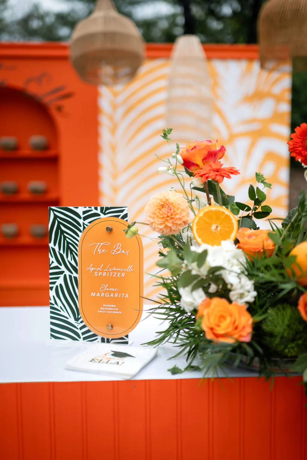 orange tropical wedding bar menu nashville private event - Nashville Private Event Catering Orange tropical themed wedding bar menu with palm leaf design and fresh floral arrangement featuring orange roses and greenery at Nashville private event by A Catered Affair