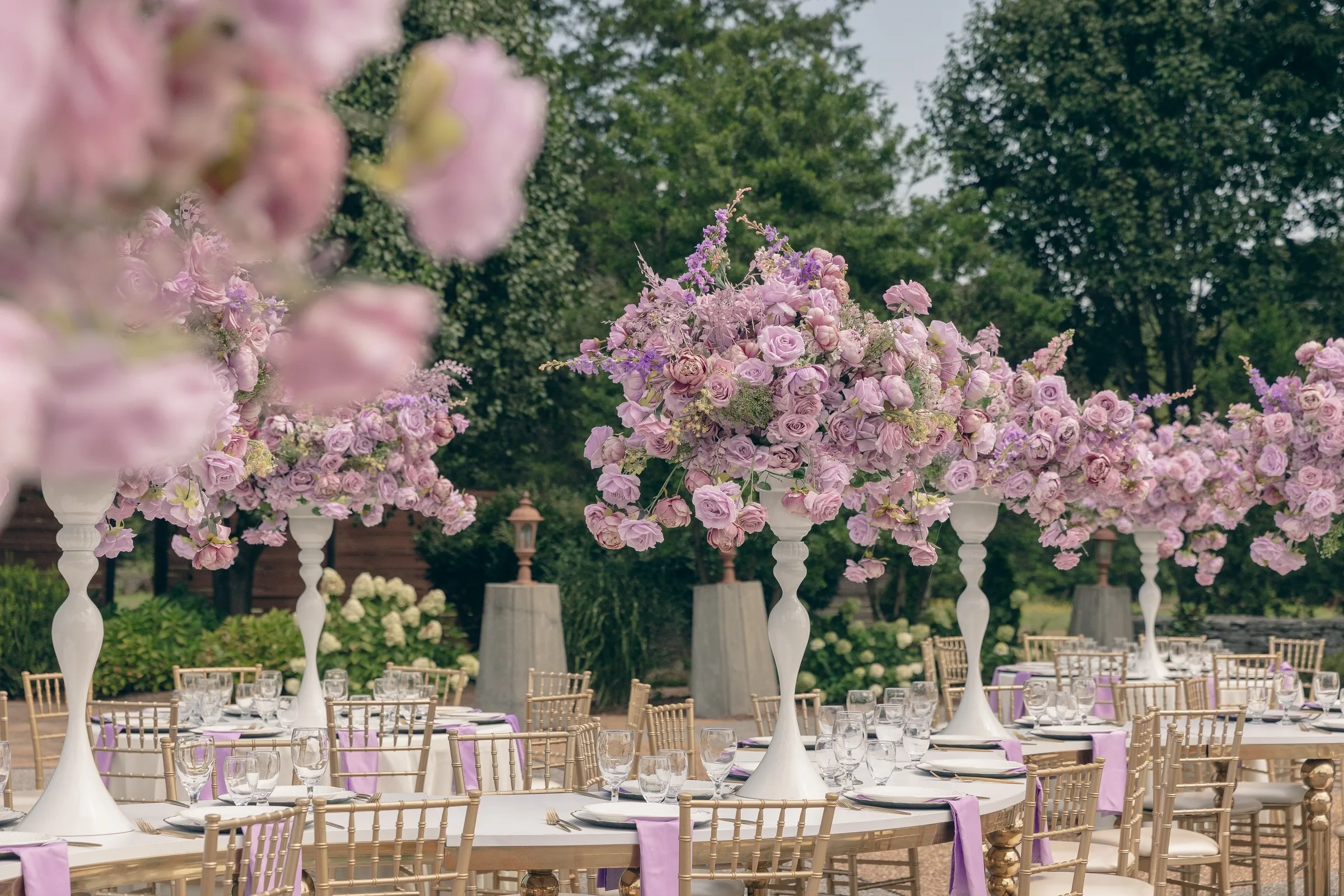purple floral centerpieces outdoor wedding reception nashville - Nashville Wedding Catering Elegant purple rose centerpieces on tall white stands at outdoor wedding reception tables with gold chiavari chairs in Nashville