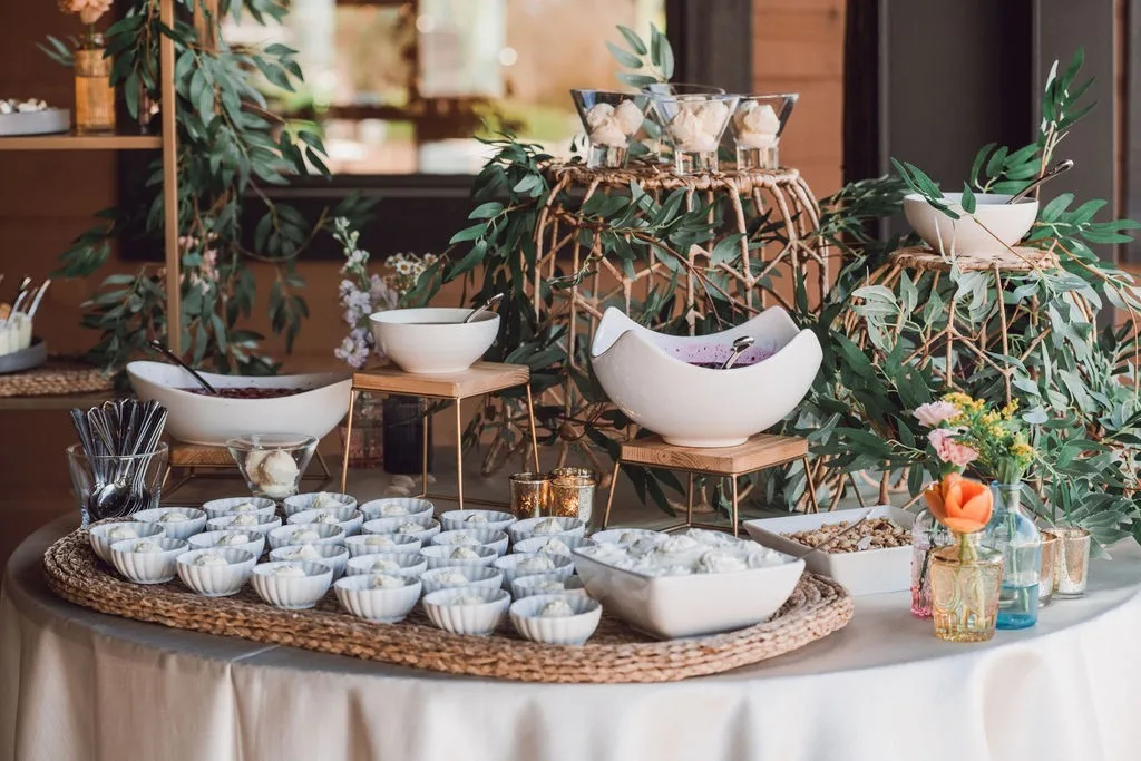 Elegant wedding catering buffet display with white serving bowls, wicker chargers, and lush greenery florals by A Catered Affair Nashville