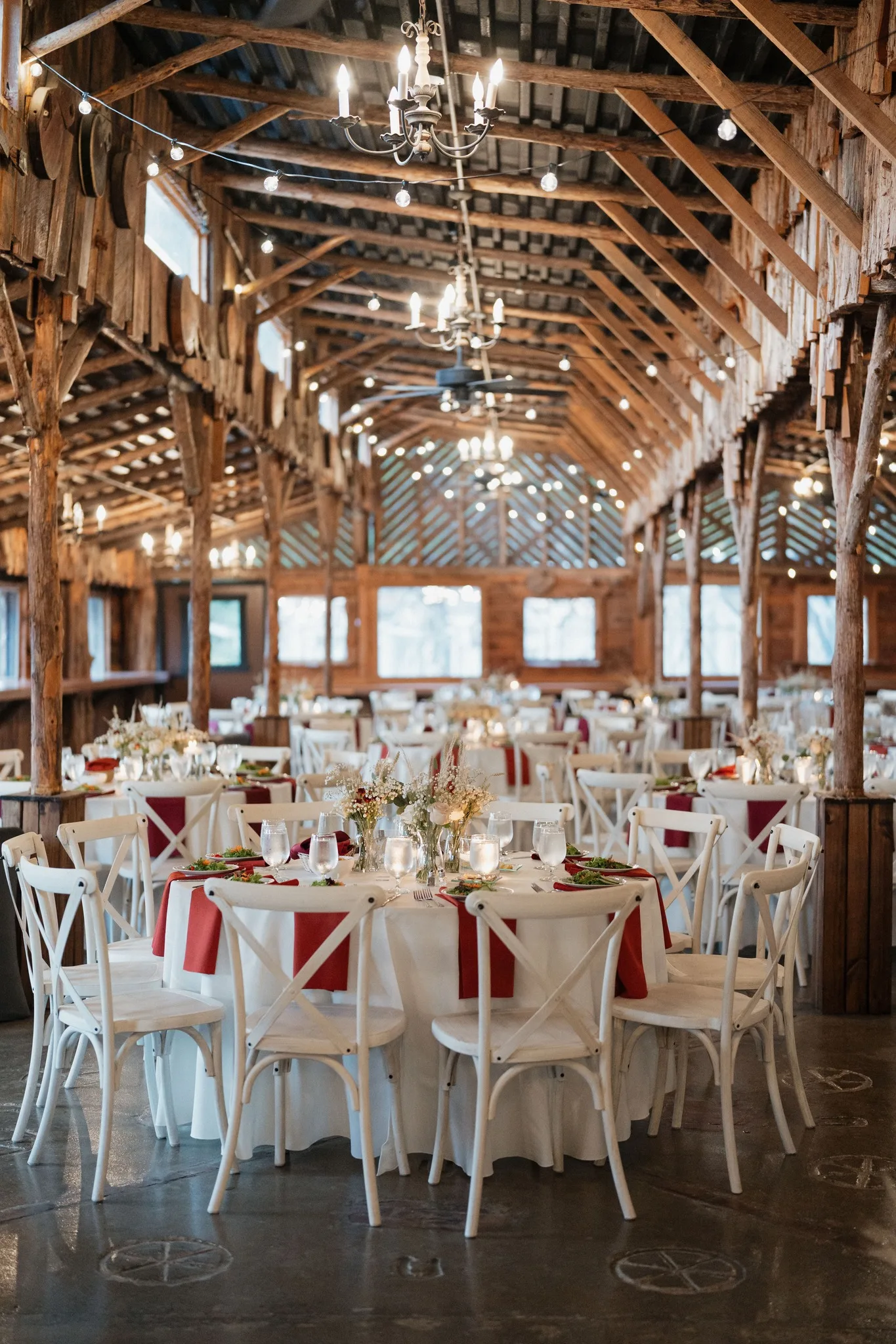 Elegant wedding reception setup with round tables, red napkins and string lights in rustic barn at Legacy Farms Nashville venue
